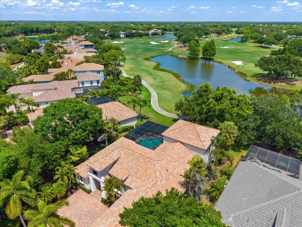 An aerial view shows a house with a screened pool overlooking a golf course pond — 7527 GREYSTONE STREET, LAKEWOOD RANCH, FL