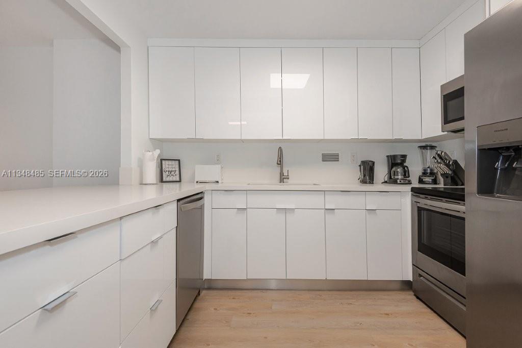 A modern kitchen features white flat-panel cabinets, stainless steel appliances, and light wood-look flooring — 2301 Collins Ave # 927, Miami Beach FL 33139, MIAMI BEACH, FL
