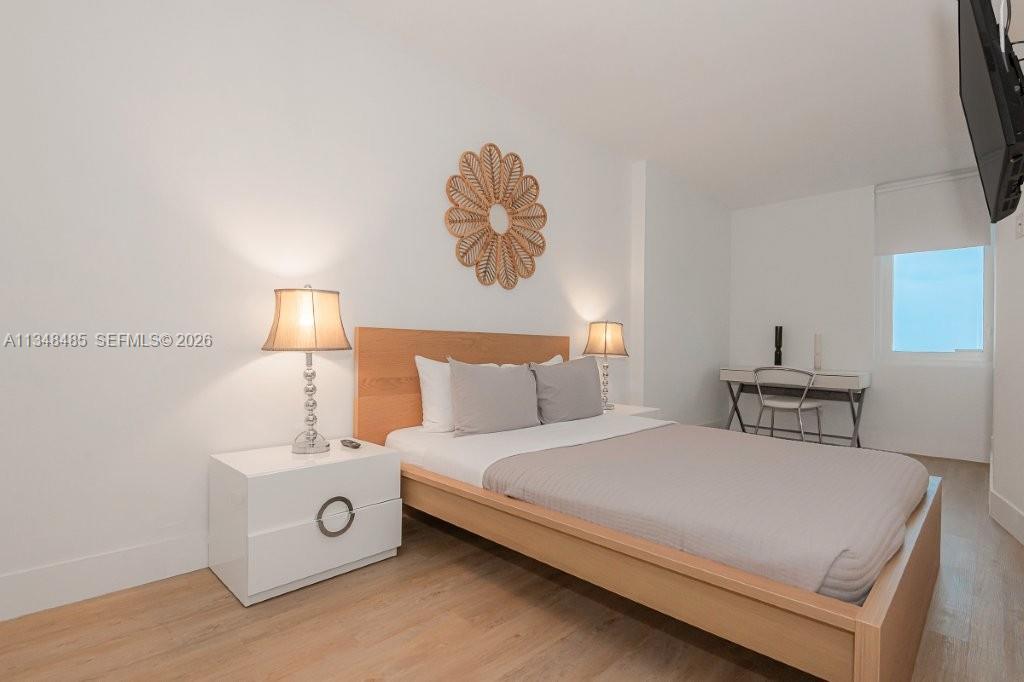 A bedroom features a wooden bed frame, white nightstands, lamps, and a desk by the window — 2301 Collins Ave # 927, Miami Beach FL 33139, MIAMI BEACH, FL