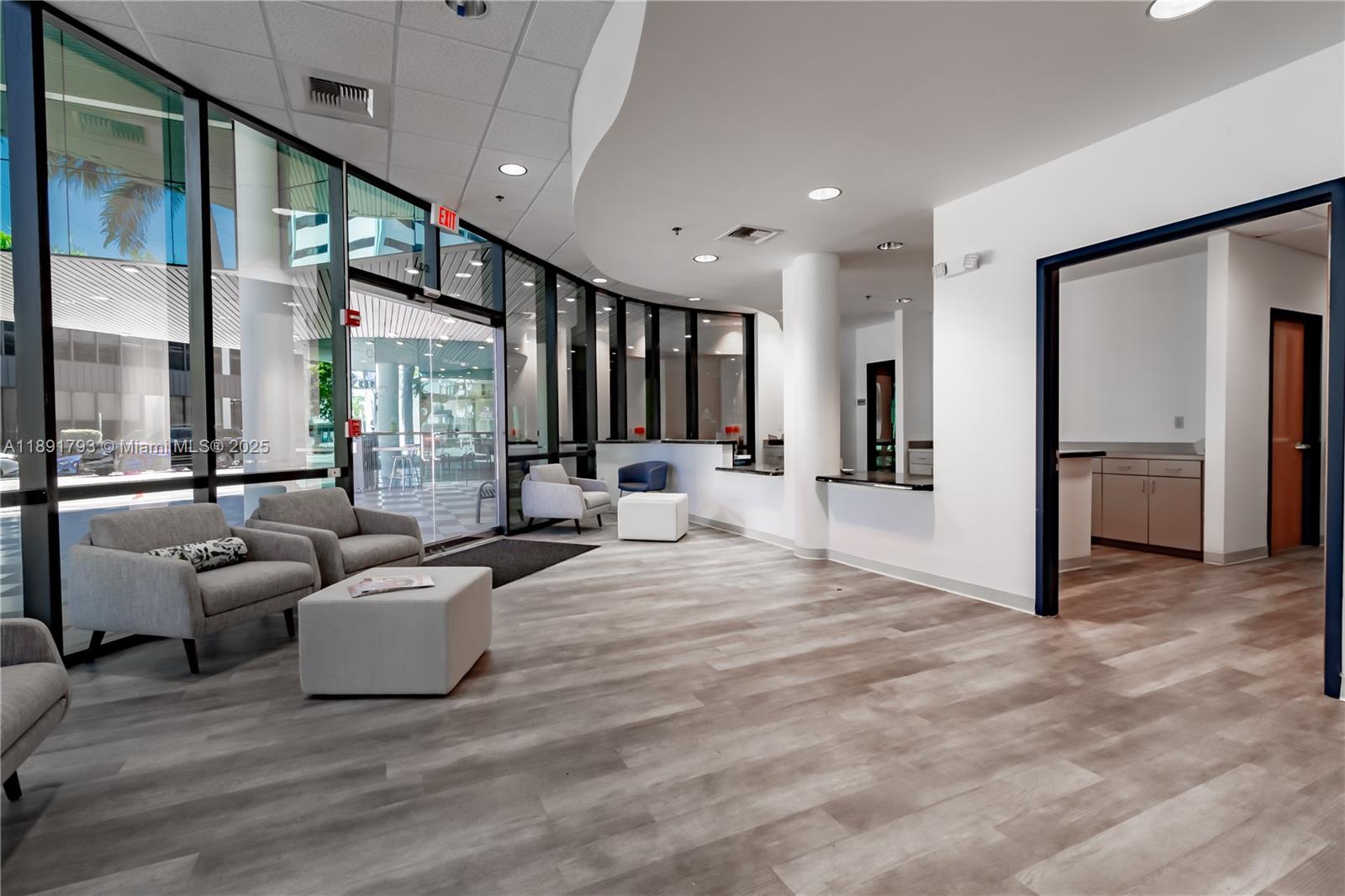 A modern office lobby features gray wood-look flooring, floor-to-ceiling windows, and a reception desk — 410 W 41st St # 103, Miami Beach FL 33140, MIAMI BEACH, FL