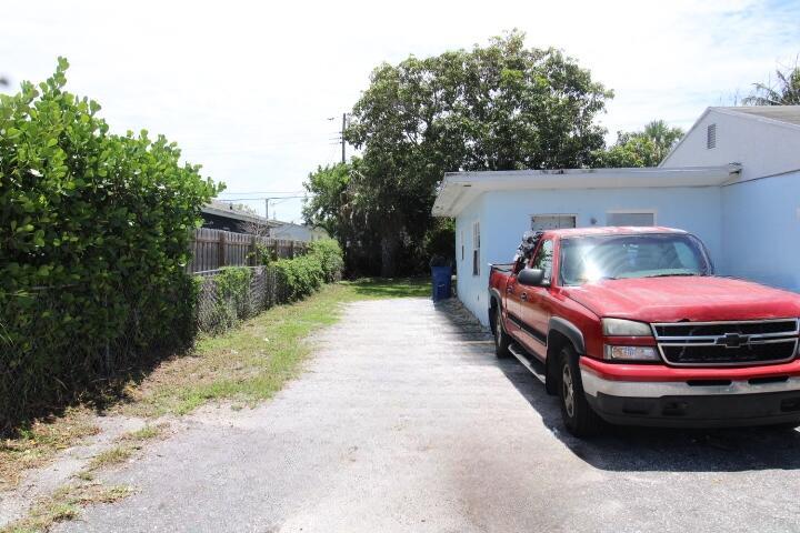 A red pickup truck is parked on a gravel driveway next to a light blue house — 1417 W 32nd Street, Riviera Beach FL 33404, RIVIERA BEACH, FL