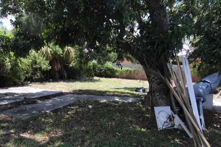 A large tree shades a grassy backyard with a concrete patio and scattered construction debris — 1417 W 32nd Street, Riviera Beach FL 33404, RIVIERA BEACH, FL