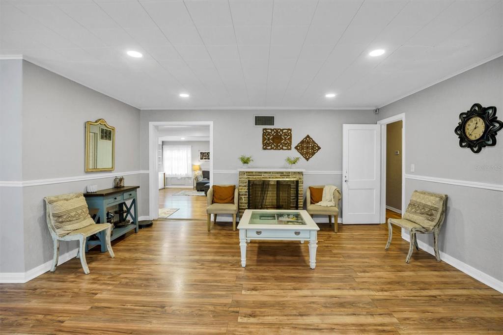 A living room features a brick fireplace, light gray walls, wood-look flooring, and recessed lighting — 615 AVENUE A NE, WINTER HAVEN, FL