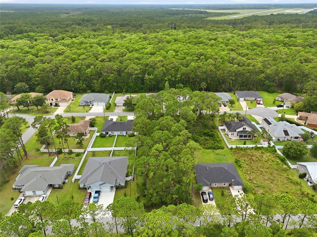 An aerial view shows suburban houses surrounded by dense forest and a nearby airport runway — 73 ULLIAN TRAIL, PALM COAST, FL