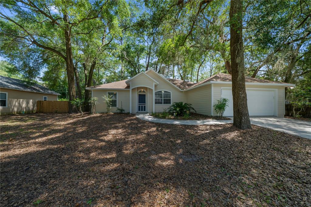 A single-story house with light siding, a two-car garage, and a tree-covered front yard — 2077 SW 42ND LANE, GAINESVILLE, FL