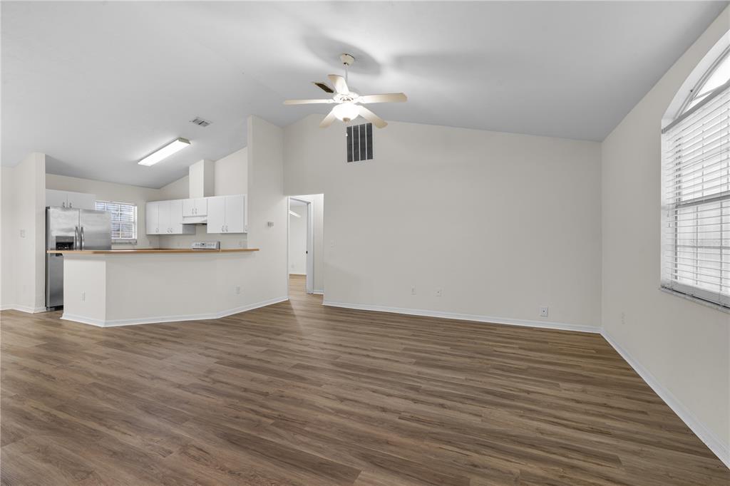 A living room with wood-look flooring, a vaulted ceiling, a ceiling fan, and an open kitchen — 2077 SW 42ND LANE, GAINESVILLE, FL
