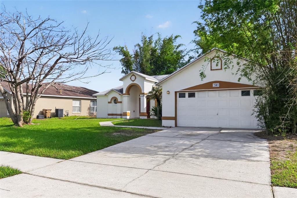 A single-story house with a white stucco exterior, brown trim, and a two-car garage — 2581 SAGE DRIVE, KISSIMMEE, FL