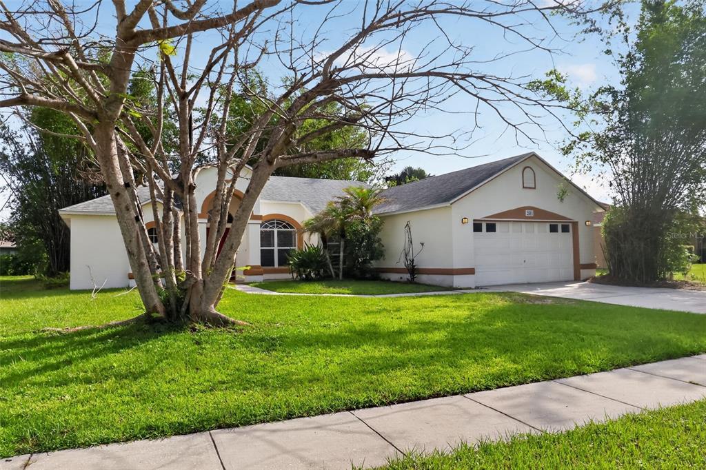 A single-story house with a white stucco exterior, a two-car garage, and a large tree — 2581 SAGE DRIVE, KISSIMMEE, FL