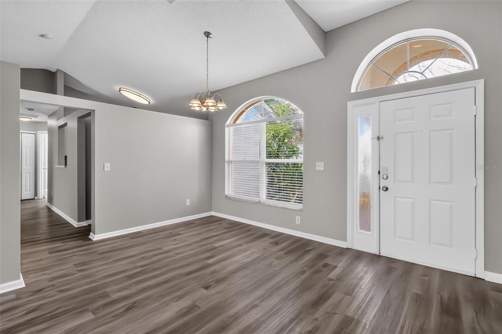 An empty room with gray walls, wood-look flooring, a chandelier, and a white front door — 2581 SAGE DRIVE, KISSIMMEE, FL