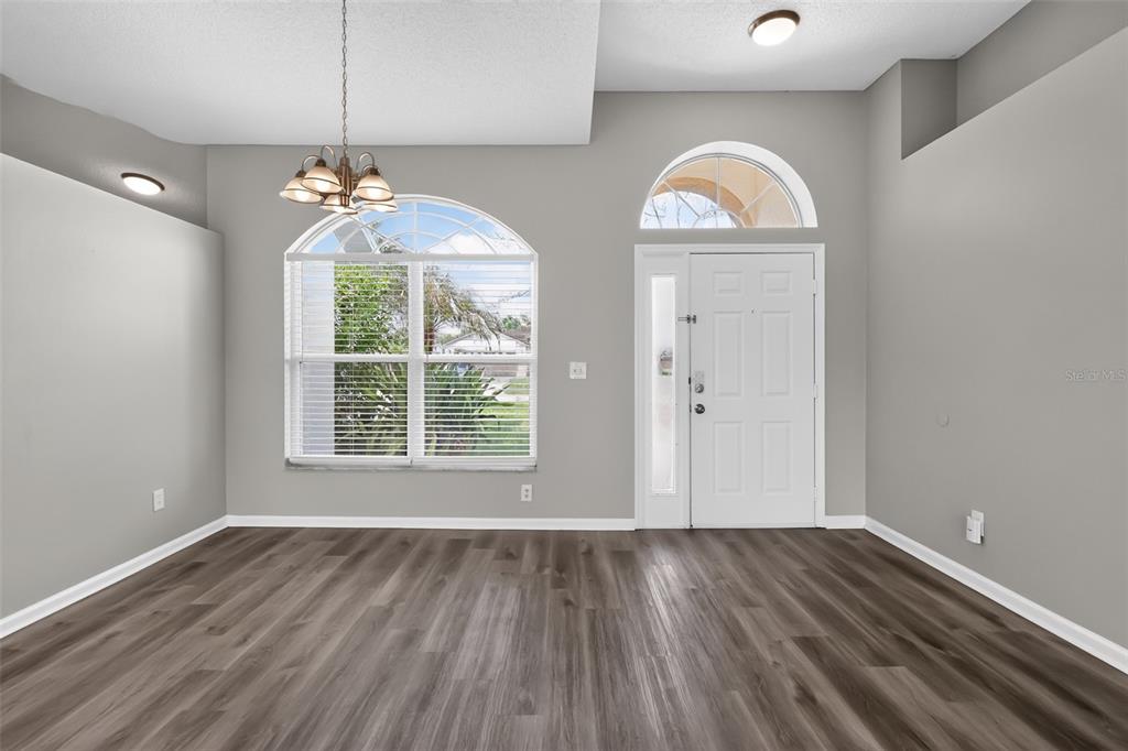 An empty room with gray walls, wood-look flooring, a large window, and a front door — 2581 SAGE DRIVE, KISSIMMEE, FL