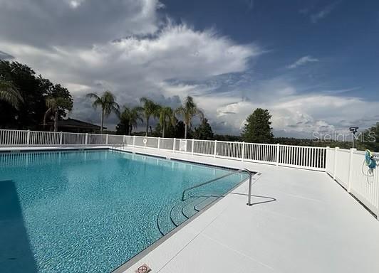 An outdoor swimming pool with a white fence and palm trees under a cloudy sky — 4916 CAPE HATTERAS DRIVE, CLERMONT, FL