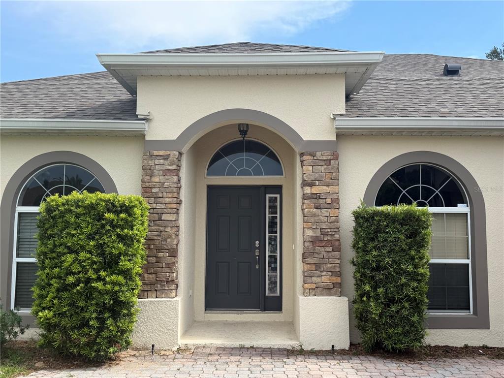 The exterior of a house features a stone-accented entryway with an arched transom window — 4916 CAPE HATTERAS DRIVE, CLERMONT, FL