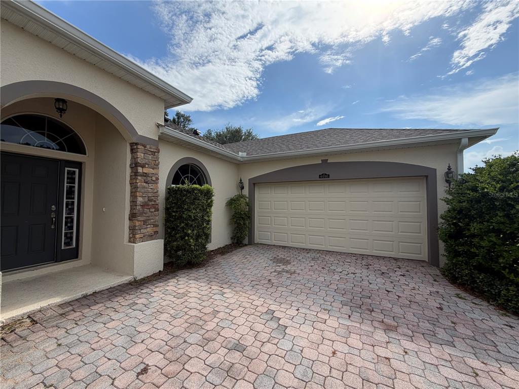 A beige house exterior features a stone-accented entryway, a two-car garage, and a paver driveway — 4916 CAPE HATTERAS DRIVE, CLERMONT, FL