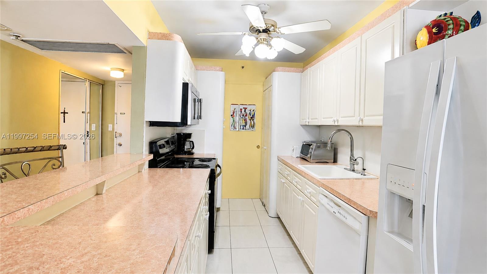 A galley kitchen features white cabinets, pink laminate countertops, and a ceiling fan — 100 Lincoln Rd # 422, Miami Beach FL 33139, MIAMI BEACH, FL