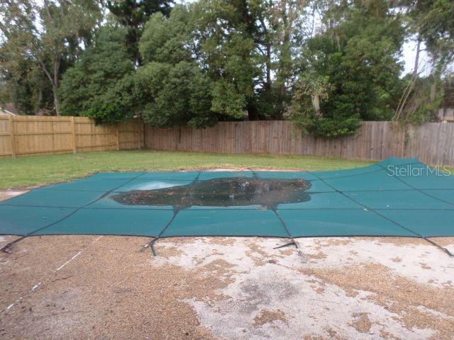 A backyard features a swimming pool covered by a green mesh safety cover — 210 BANBURY COURT, LONGWOOD, FL