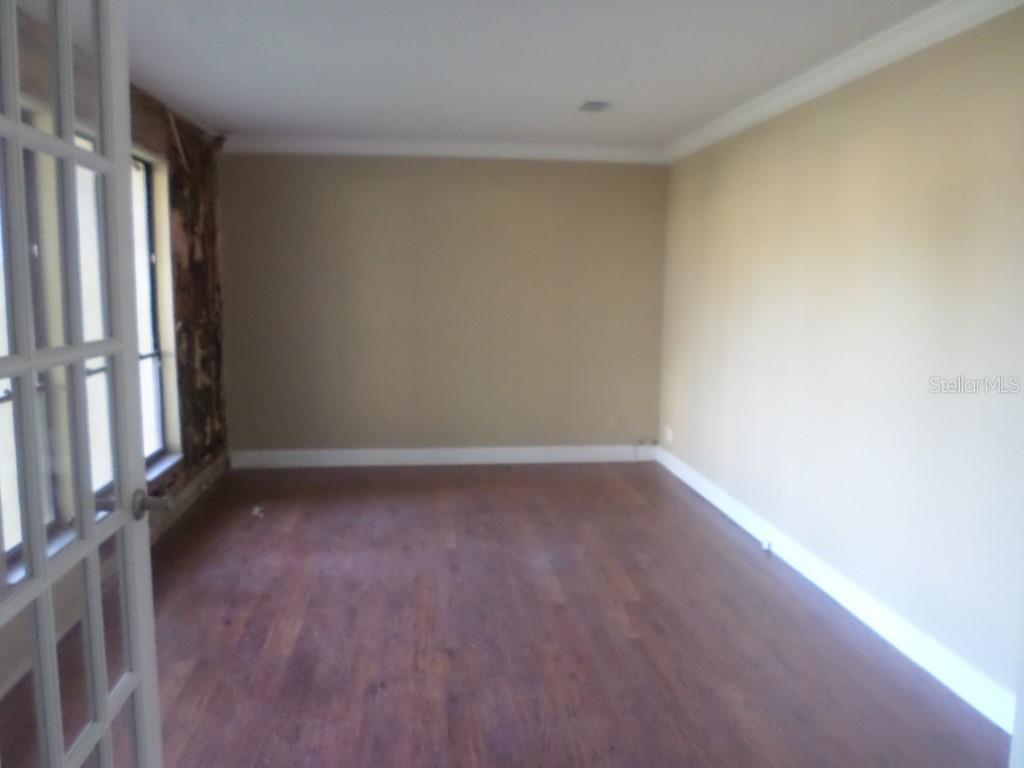 An empty room features dark wood flooring, beige walls, crown molding, and a French door — 210 BANBURY COURT, LONGWOOD, FL