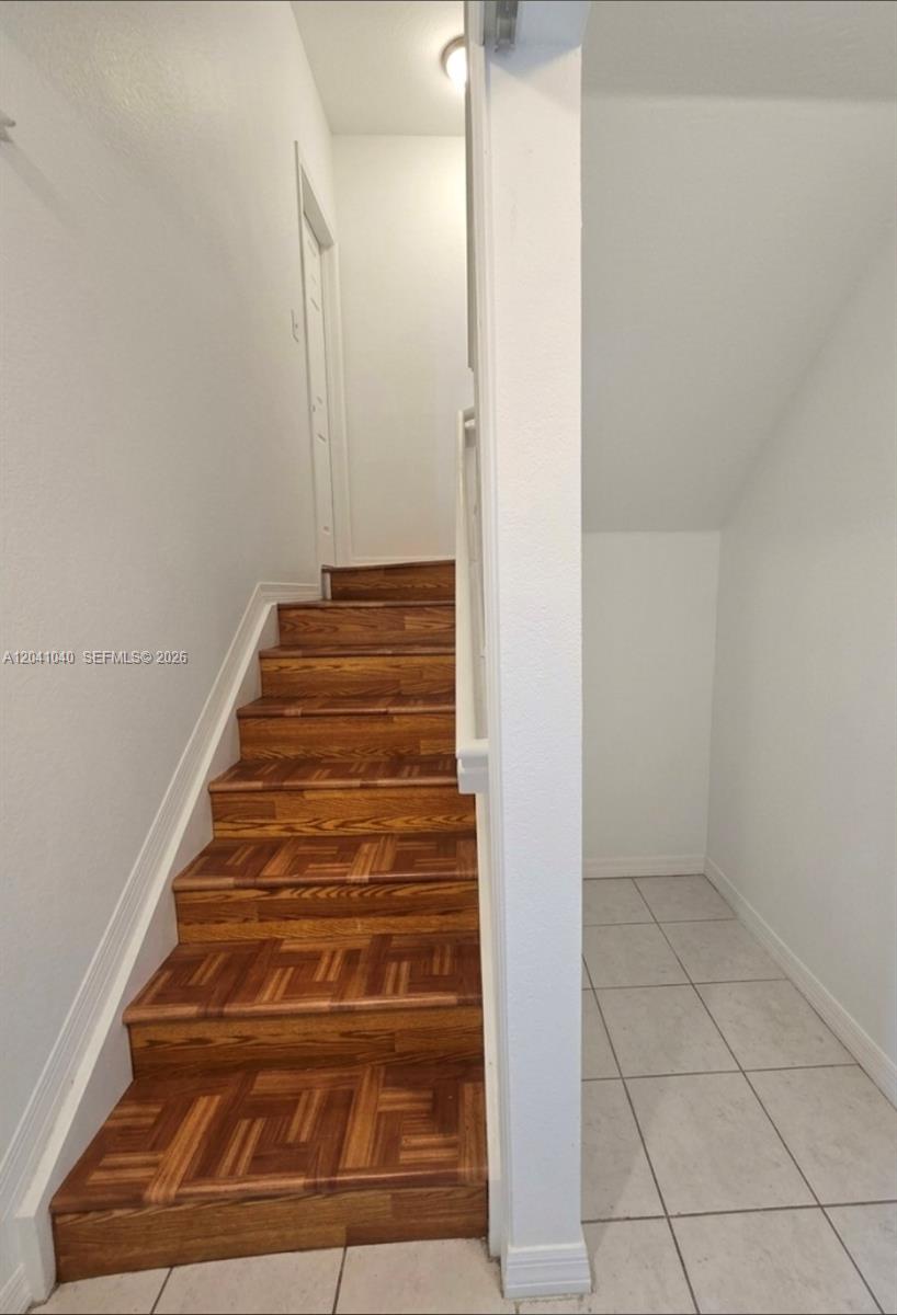 A wooden staircase with a parquet pattern leads upward next to a tiled alcove — 8936 W Flagler St # 204, Miami FL 33174, MIAMI, FL