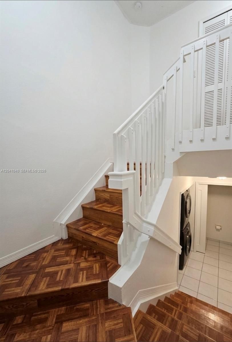 A wooden staircase with parquet treads leads upward next to a white railing and laundry — 8936 W Flagler St # 204, Miami FL 33174, MIAMI, FL