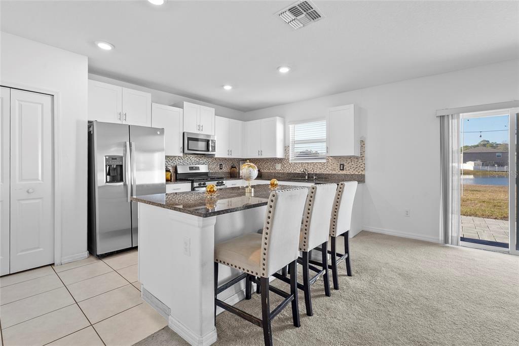 A kitchen features white cabinets, stainless steel appliances, a granite island, and a sliding glass door — 4016 86TH STREET E, PALMETTO, FL