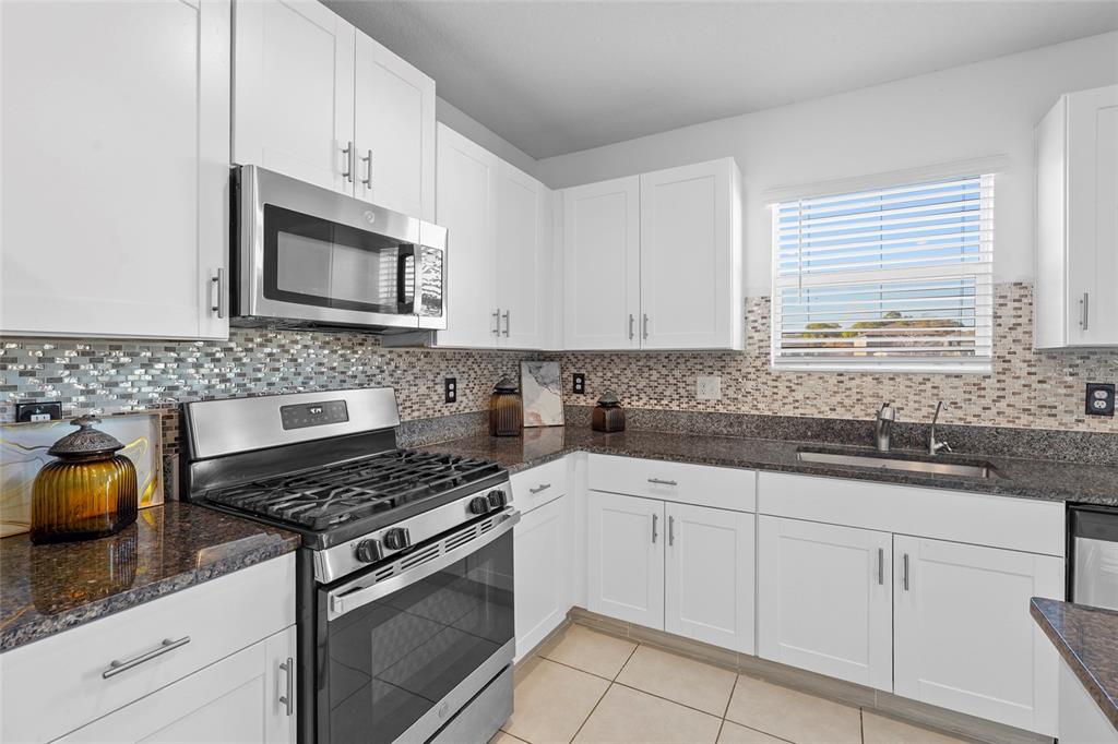 A kitchen features white cabinets, granite countertops, a stainless steel stove, and a mosaic backsplash — 4016 86TH STREET E, PALMETTO, FL