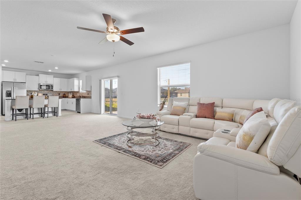 A bright, open-concept living room and kitchen featuring white cabinetry, carpeted floors, and white furniture — 4016 86TH STREET E, PALMETTO, FL