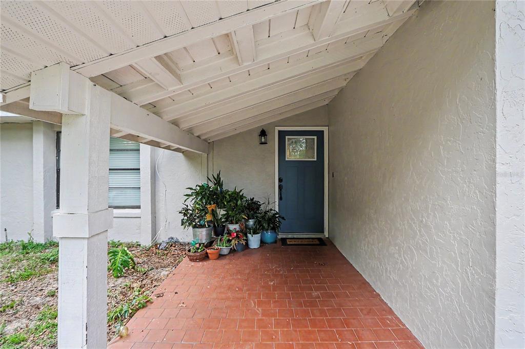 A covered porch features red tile flooring, a blue front door, and several potted plants — 20250 SW 93 LANE ROAD, DUNNELLON, FL