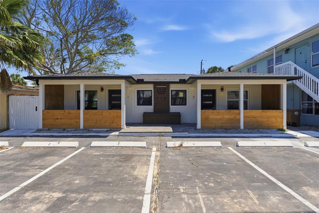 A single-story building with two covered porches, wood-slat railings, and a paved parking lot — 113 145TH AVENUE E UNIT 4, MADEIRA BEACH, FL