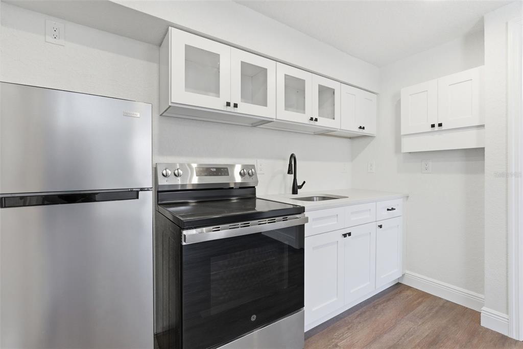 A kitchen features white cabinets, stainless steel appliances, a black faucet, and wood-look flooring — 113 145TH AVENUE E UNIT 4, MADEIRA BEACH, FL