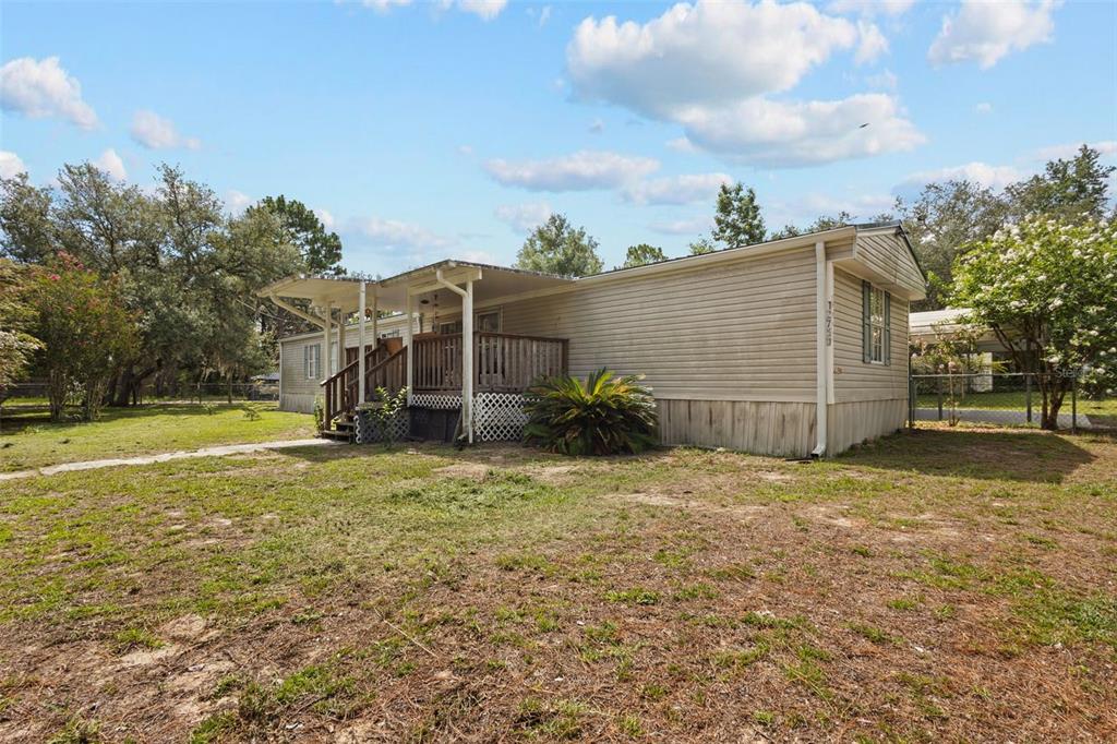 A single-story mobile home with beige siding, a wooden deck, and a metal carport roof — 12750 NE 65TH STREET, WILLISTON, FL