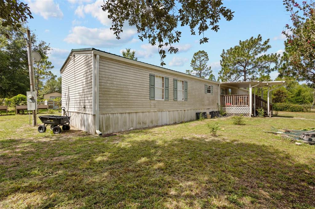 Exterior view of a single-wide mobile home with light siding and a wooden deck — 12750 NE 65TH STREET, WILLISTON, FL