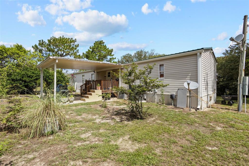 A single-story manufactured home with a covered porch and beige siding sits on a grassy lot — 12750 NE 65TH STREET, WILLISTON, FL
