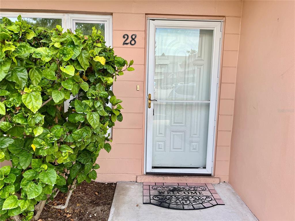 A front entrance with a white storm door, house number 28, and a welcome mat — 2458 COLUMBIA DRIVE UNIT 28, CLEARWATER, FL