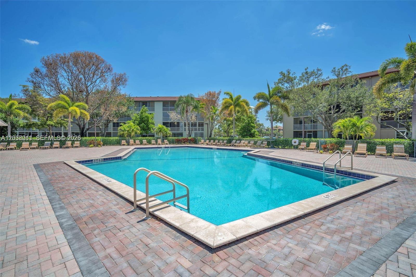 A rectangular swimming pool is surrounded by a brick patio and lounge chairs — PEMBROKE PINES, FL