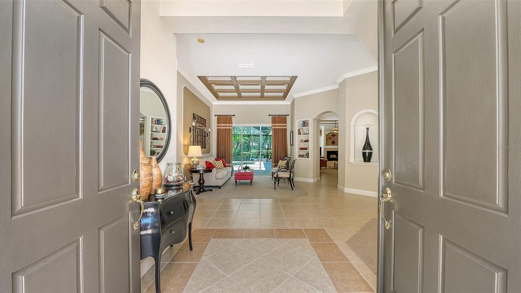 A view through an open front door into a tiled foyer leading to a living room — 7507 ABBEY GLEN, BRADENTON, FL