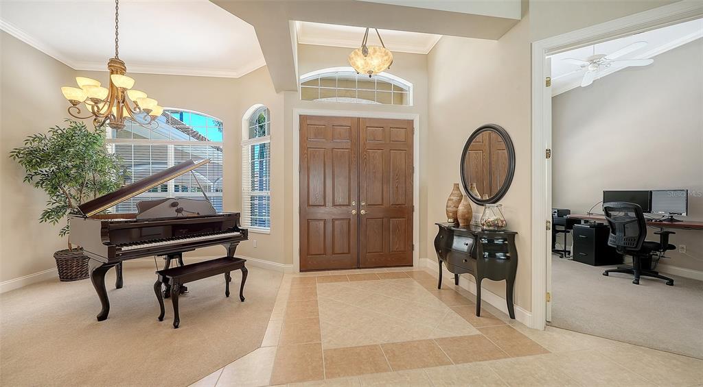 A grand foyer features a baby grand piano, tile flooring, and double wooden entry doors — 7507 ABBEY GLEN, BRADENTON, FL