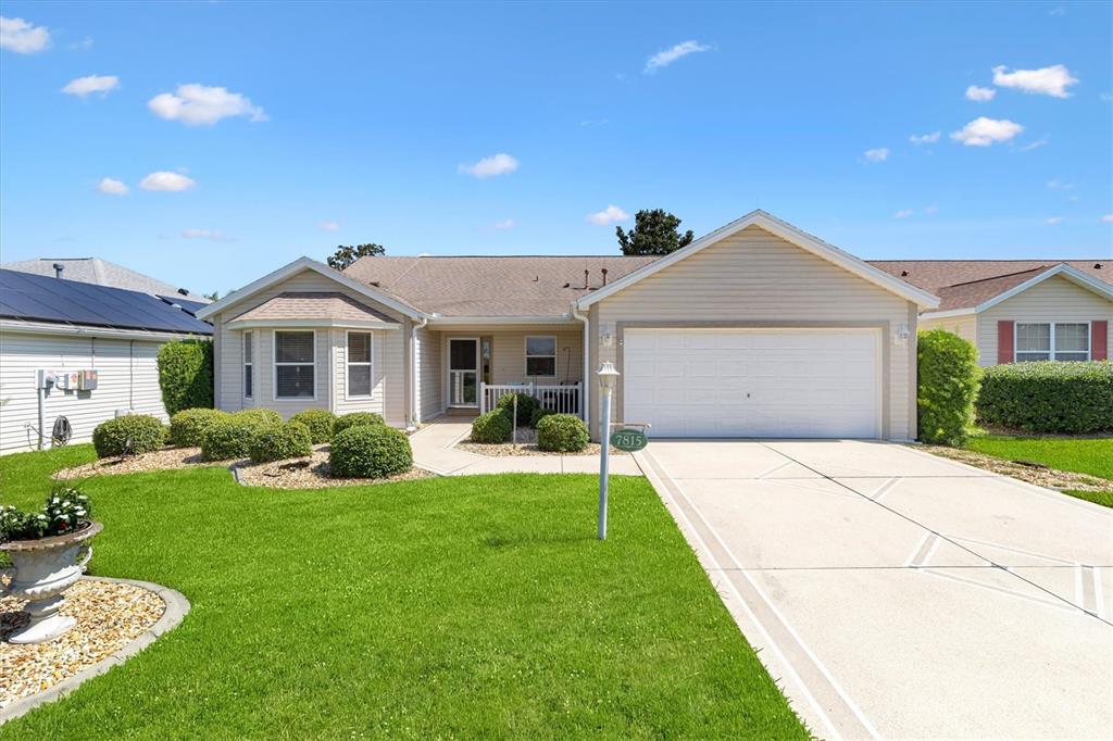 A single-story house with beige siding, a two-car garage, and a manicured front lawn — 7815 SE 166TH HIBERNIA LANE, THE VILLAGES, FL