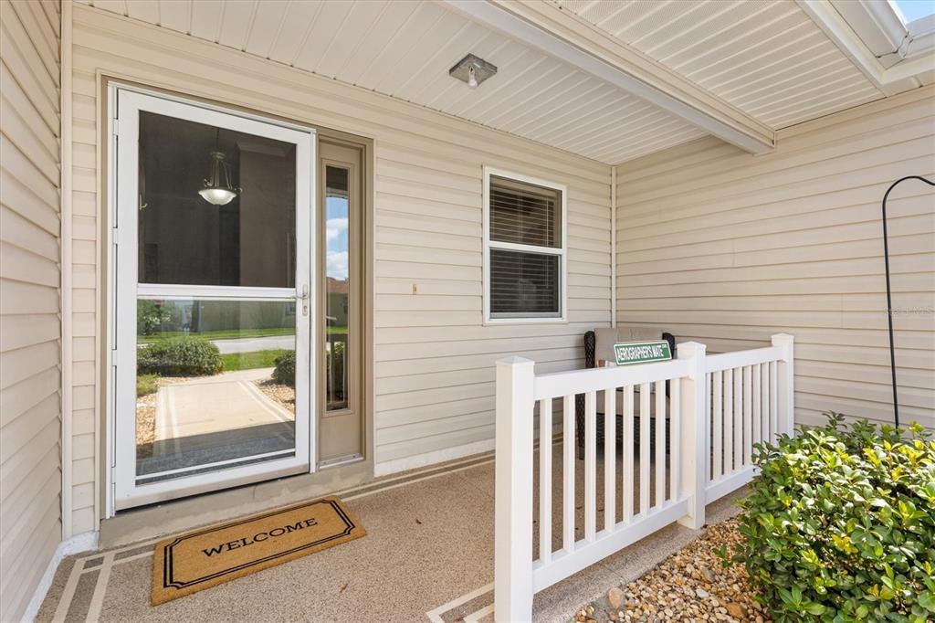 A covered front porch features beige vinyl siding, a white railing, and a welcome mat — 7815 SE 166TH HIBERNIA LANE, THE VILLAGES, FL