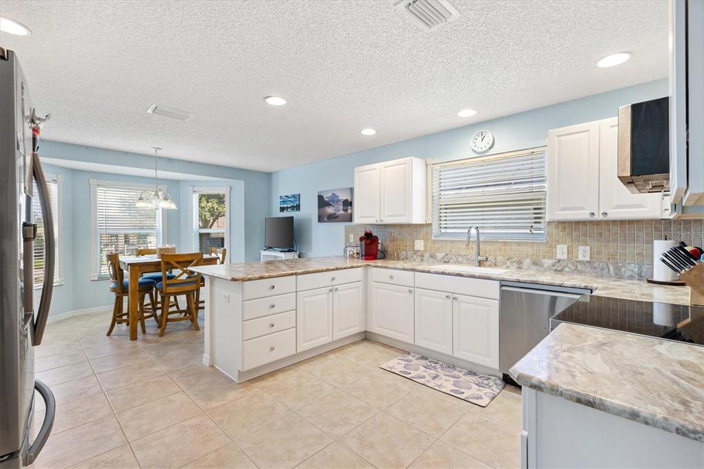A kitchen with white cabinets, marble-look countertops, stainless steel appliances, and an adjacent dining area — 7815 SE 166TH HIBERNIA LANE, THE VILLAGES, FL
