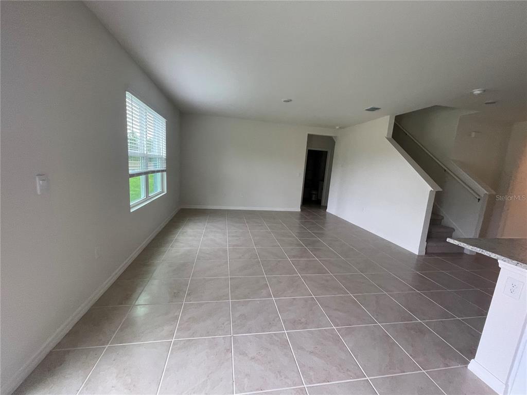 An empty living area features light-colored tile flooring, white walls, and a staircase — 498 BARONESS WAY, DELAND, FL