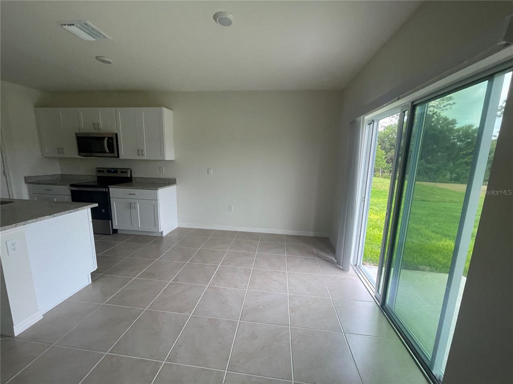 A kitchen with white cabinets and tile flooring opens to a patio through sliding doors — 498 BARONESS WAY, DELAND, FL