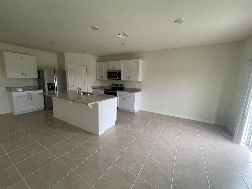 A kitchen features white cabinets, granite countertops, a center island, and light-colored tile flooring — 498 BARONESS WAY, DELAND, FL