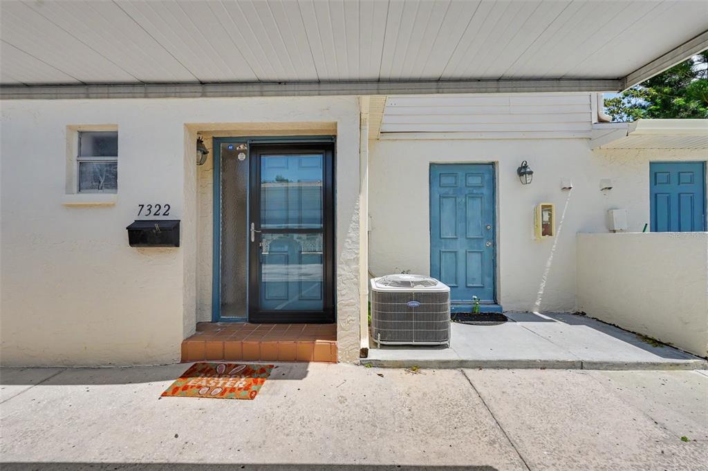 The exterior of a home features a covered patio, two blue doors, and an air conditioner — 7322 STONE HAVEN COURT N UNIT 7322, PINELLAS PARK, FL