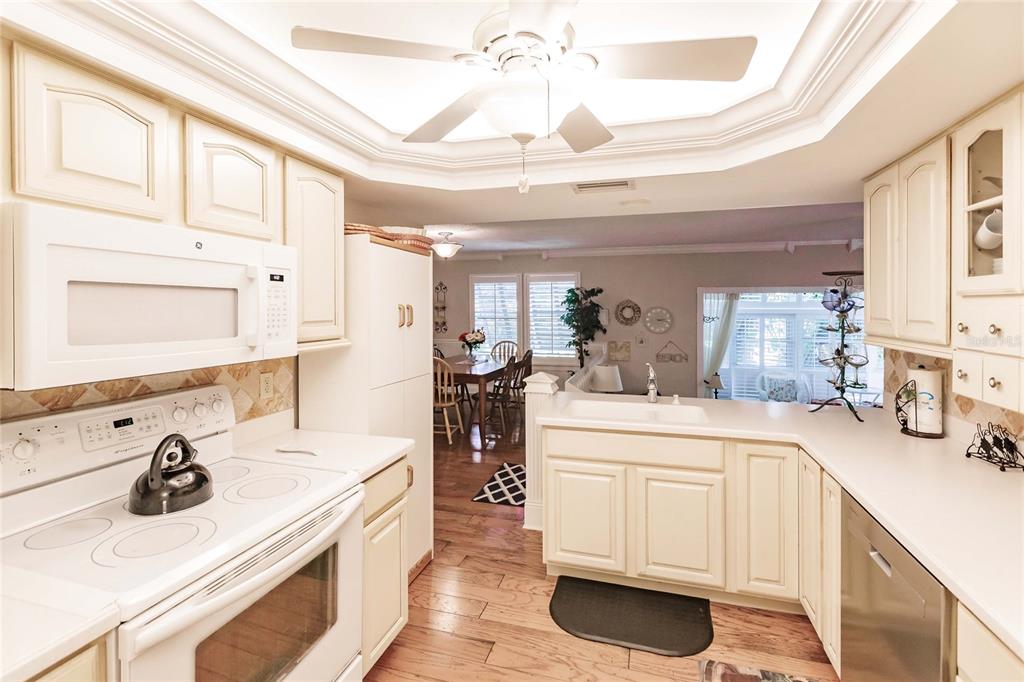 A kitchen with white cabinets, white appliances, and a ceiling fan overlooks a dining area — 6030 E PEPPERTREE WAY UNIT 222A, SARASOTA, FL