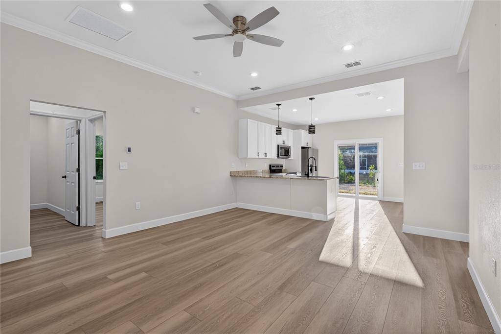 An open-concept living area with light wood flooring, a ceiling fan, and a kitchen — 661 NE 150TH COURT, WILLISTON, FL