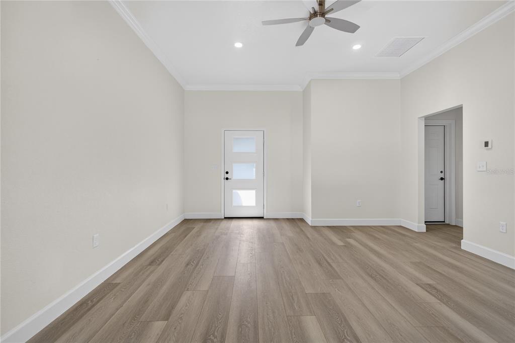 An empty room features light wood-look flooring, white walls, a ceiling fan, and two doors — 661 NE 150TH COURT, WILLISTON, FL