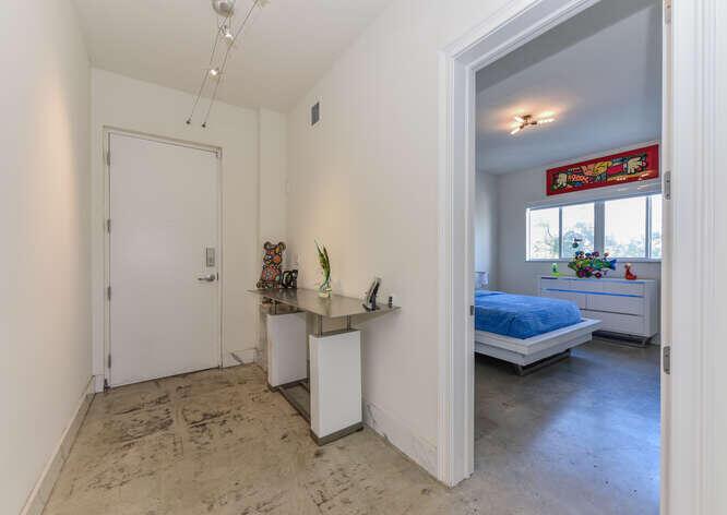 A hallway with a console table leads into a bedroom with a blue bed — 108 Lake Avenue # 406, FL 33460, FL