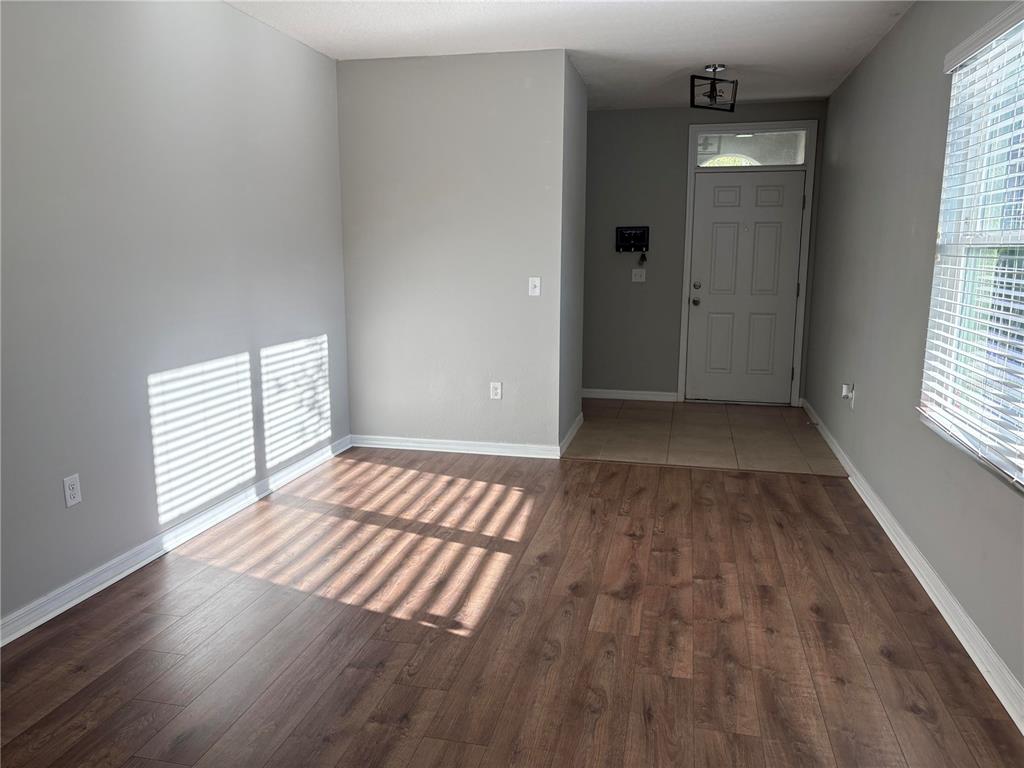 An empty room with wood-look flooring, gray walls, a front door, and window blinds — 10104 HAWK STORM AVENUE, TAMPA, FL