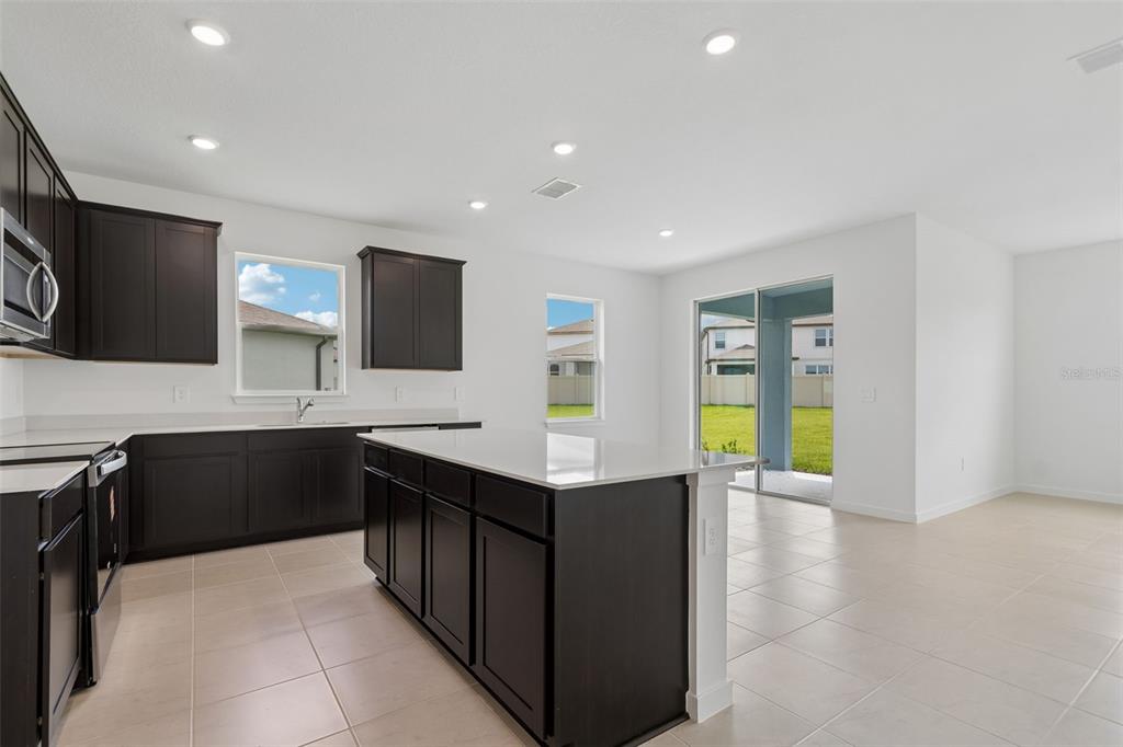A modern kitchen features dark cabinetry, white countertops, a central island, and tile flooring — 11243 SYCAMORE GLEN LOOP, THONOTOSASSA, FL
