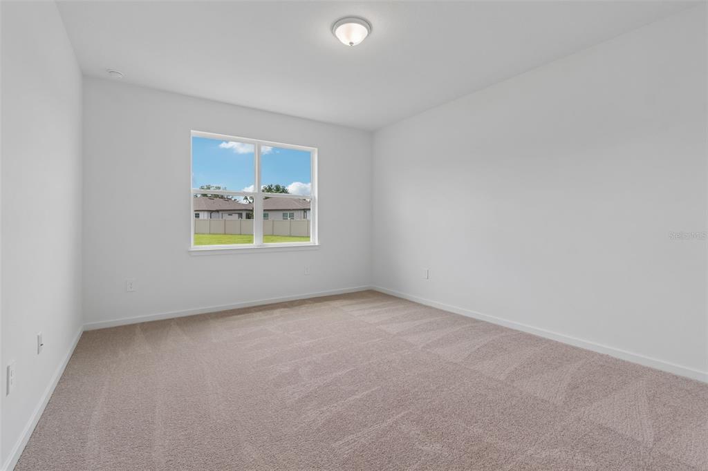 An empty bedroom features white walls, beige carpeting, and a single window overlooking a yard — 11243 SYCAMORE GLEN LOOP, THONOTOSASSA, FL