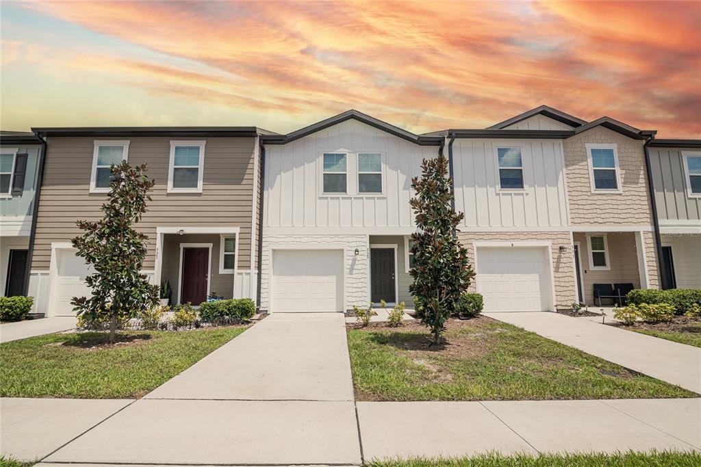 A row of three modern townhomes with attached garages and driveways under a sunset sky — 529 MADISON DRIVE, DAVENPORT, FL